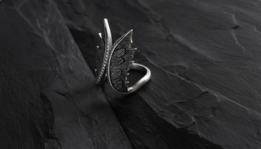 Side view of handcrafted angel wings ring showing detailed feather texture and open band design on black stone