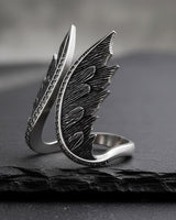 Close-up of sterling silver angel wings ring with intricate metalwork and sparkling gems on textured surface