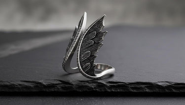 Close-up of sterling silver angel wings ring with intricate metalwork and sparkling gems on textured surface