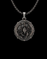 Detailed silver scorpion pendant with an oxidized finish, featuring a central scorpion and ornate gothic border on a chain.
