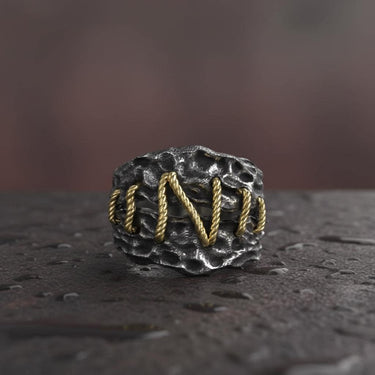 Close-up of Frankenstein ring displaying intricate golden wire stitching pattern on weathered silver surface