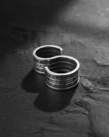 Silver spell ring with engraved runes in an S-shape design, displayed on a dark, textured stone surface for dramatic effect.