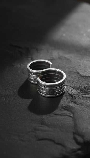 Silver spell ring with engraved runes in an S-shape design, displayed on a dark, textured stone surface for dramatic effect.