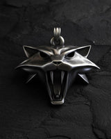 Silver Witcher Cat School medallion with a fierce, snarling expression and bared fangs, laid flat on a dark slate surface.