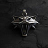 Silver Witcher Cat School medallion with a fierce, snarling expression and bared fangs, laid flat on a dark slate surface.