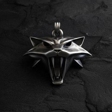Silver Witcher Cat School medallion with a fierce, snarling expression and bared fangs, laid flat on a dark slate surface.