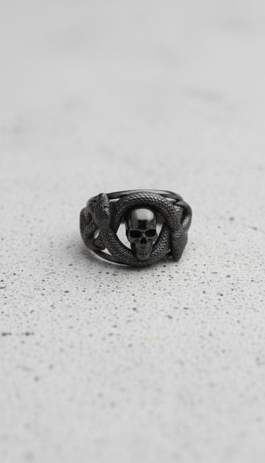 Black rhodium plated silver snake skull ring featuring a double headed serpent wrapping a skull on a textured surface