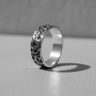 Black and white photo of a Moon Surface Silver Ring with a heavily cratered, hammered texture, standing on a light surface.