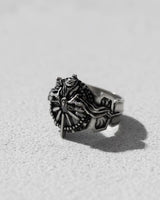 Three-quarter angle of the Silver Ring of Lucii, highlighting the intricate sculptural details and band depth on a light surface.