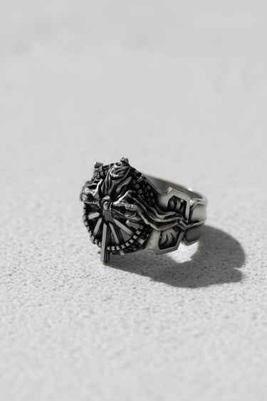 Three-quarter angle of the Silver Ring of Lucii, highlighting the intricate sculptural details and band depth on a light surface.