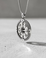Men's silver compass pendant on a sterling silver snake chain, shown hanging at an angle to display its 3D depth.