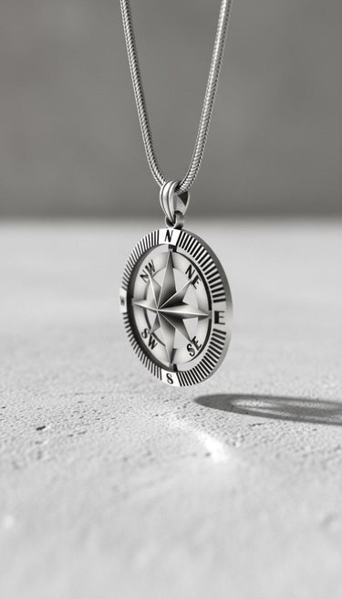 Men's silver compass pendant on a sterling silver snake chain, shown hanging at an angle to display its 3D depth.
