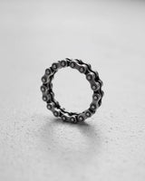 Sterling silver bike chain ring with an oxidized finish, standing on a light gray textured surface to show its detail.