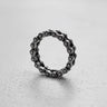 Sterling silver bike chain ring with an oxidized finish, standing on a light gray textured surface to show its detail.