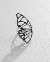 Silver butterfly wing ring with a delicate openwork design, resting on a white textured surface showing its fine craftsmanship.