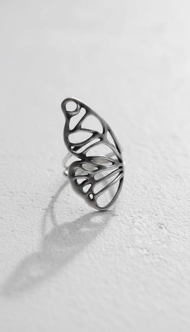 Silver butterfly wing ring with a delicate openwork design, resting on a white textured surface showing its fine craftsmanship.