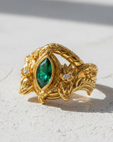 Yellow gold vermeil dragon ring featuring two detailed dragon heads and a central green gem, shot in bright sunlight.