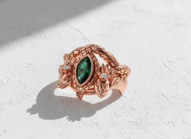 Artisan rose gold vermeil dragon ring with intricate scale details and a vibrant emerald, displayed on a clean white background.