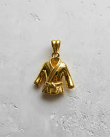 Yellow gold plated Karate Gi pendant displaying the shiny finish of the lapels and sleeves, shot top-down against a white wall.