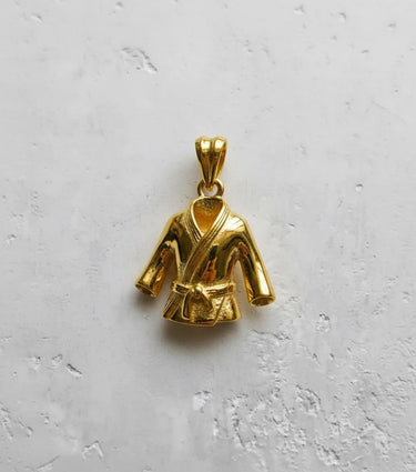 Yellow gold plated Karate Gi pendant displaying the shiny finish of the lapels and sleeves, shot top-down against a white wall.