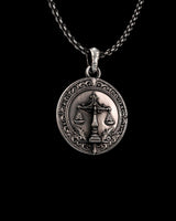 Angled close-up of the silver Scales of Justice pendant, highlighting the oxidized finish and intricate details of the central scales emblem.