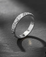 A sterling silver carved wedding band with a bright polished finish, showing the detailed botanical vine engraving on stone.