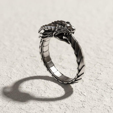 Silver Ouroboros dragon ring with detailed scales on a textured white surface, showing the intricate head design biting its tail.