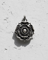 Oxidized 925 silver Tudor Rose Pendant showing detailed layered petals and thorns, casting a shadow on a white wall.