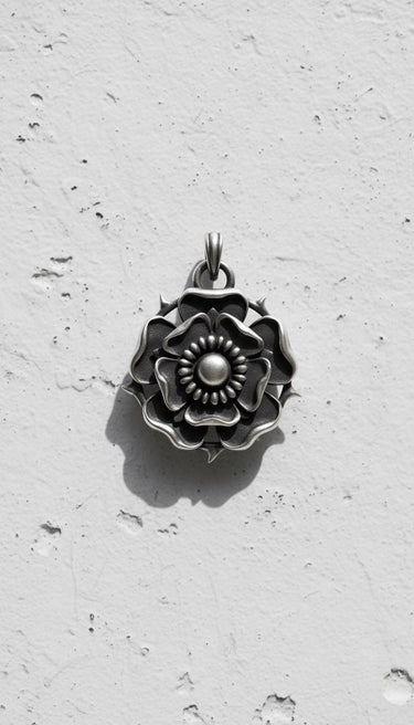 Oxidized 925 silver Tudor Rose Pendant showing detailed layered petals and thorns, casting a shadow on a white wall.