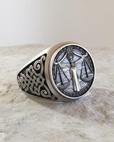 Angled view of the handcrafted silver Libra ring highlighting the intricate scrollwork on the band against a stone background.