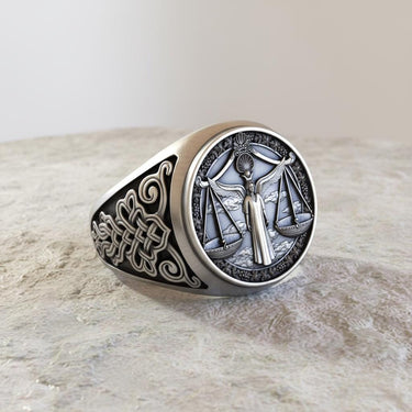 Angled view of the handcrafted silver Libra ring highlighting the intricate scrollwork on the band against a stone background.