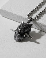 Oxidized 925 sterling silver wolf pendant shown at an angle, detailing the wolf clenching a dagger in its teeth.