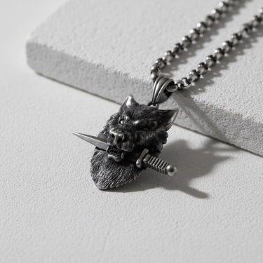 Oxidized 925 sterling silver wolf pendant shown at an angle, detailing the wolf clenching a dagger in its teeth.