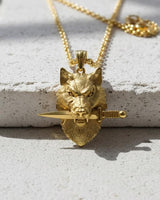 Gold-plated version of the wolf and knife pendant, showcasing the polished finish and sharp details on the dagger.