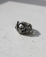 Side angle of gothic sterling silver ring with snake and skull design on textured grey background