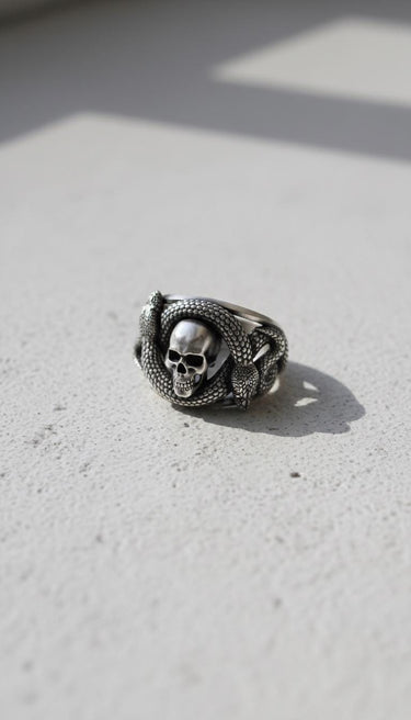 Side angle of gothic sterling silver ring with snake and skull design on textured grey background