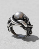 Handcrafted silver octopus ring with detailed tentacles and suckers wrapping around a large silver pearl on a light grey surface.