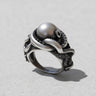 Handcrafted silver octopus ring with detailed tentacles and suckers wrapping around a large silver pearl on a light grey surface.
