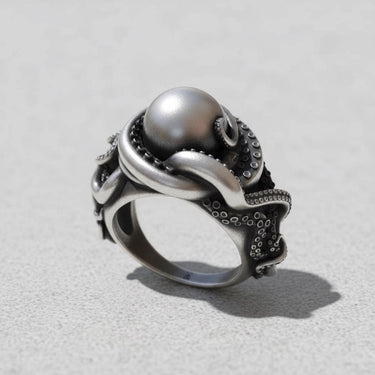 Handcrafted silver octopus ring with detailed tentacles and suckers wrapping around a large silver pearl on a light grey surface.