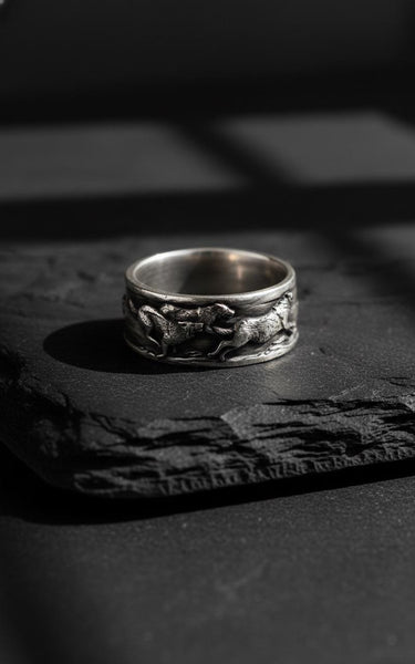 Handcrafted Silver Wolf Ring with a detailed pack of running wolves, shown in a close-up on a dark slate surface.