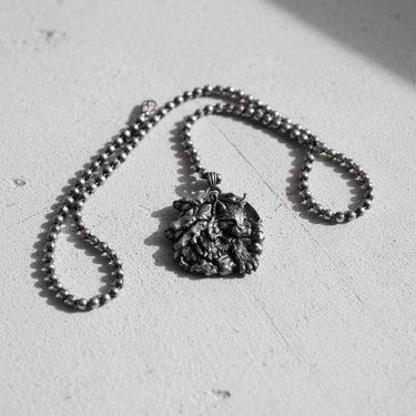 Silver lynx pendant on a ball chain, showcased on a textured white surface with artistic shadows from natural light.