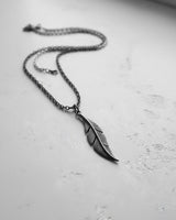 Full view of the sterling silver feather pendant necklace laid out at an angle, showing the rolo chain and its bohemian style.