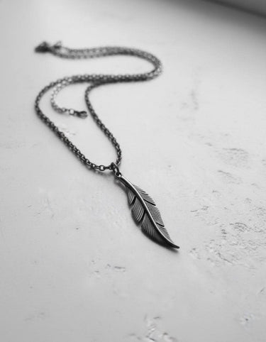 Full view of the sterling silver feather pendant necklace laid out at an angle, showing the rolo chain and its bohemian style.