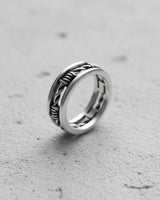 Silver barbed wire ring with a detailed, twisted wire design, shown at an angle on a light gray textured surface.