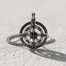 Handmade silver compass pendant with North Star design and cardinal points, lying flat on a textured white surface.