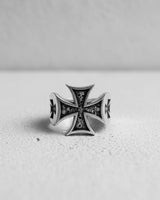Front view of the Silver Maltese Cross Ring showcasing the detailed skull engravings, set on a bright, textured surface.