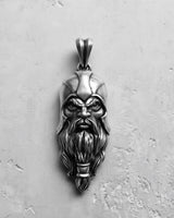 Silver Viking head pendant with an oxidized finish, showcasing the warrior's detailed face and helmet on a grey surface.
