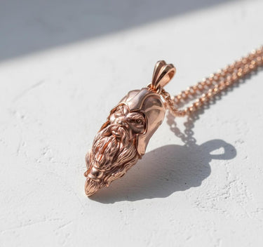 Rose gold Viking head pendant worn on a chain, showing its size and intricate design in natural side lighting.