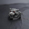 Men's silver tiger ring with detailed oxidized stripes and red gemstone eyes, shown at an angle on a dark slate surface.
