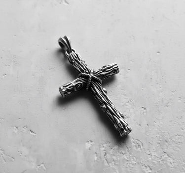 Oxidized Silver Wood Cross Pendant with detailed rope and grain texture, shown on a light grey concrete background.